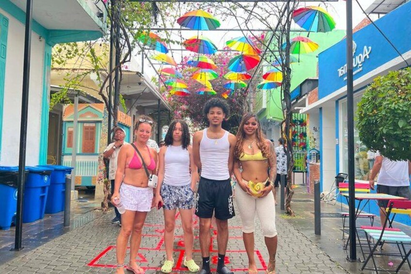 Un groupe de personnes se tient dans une rue pavée, des parapluies colorés les protégeant du soleil. 3