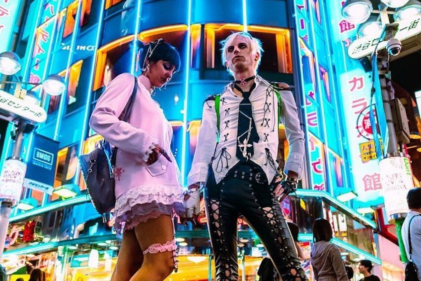 Deux personnes dans un environnement urbain animé, avec des enseignes lumineuses et des publicités. 1