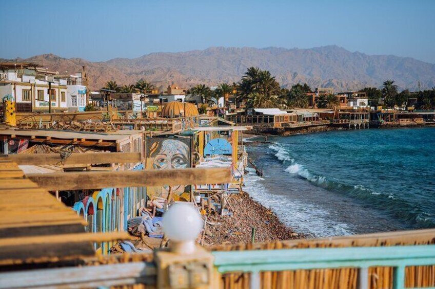 A coastal town with a beach, wooden structures, and mountains in the background. 3
