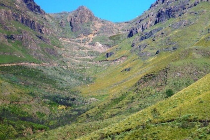 A mountainous landscape with a valley, rocky outcrops, and sparse vegetation. 4