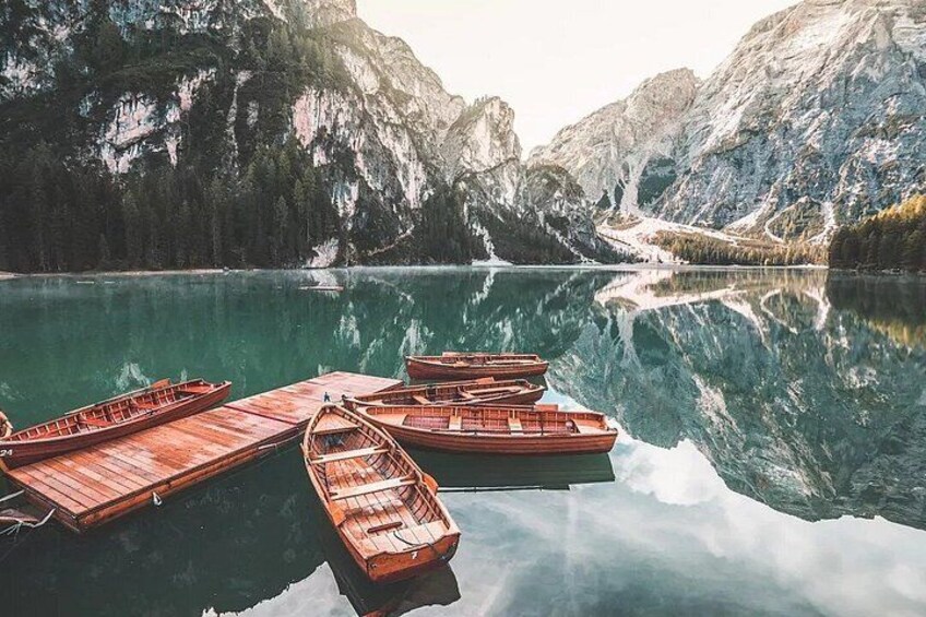 A calm lake with wooden boats docked on the shore, surrounded by mountains and trees. 4