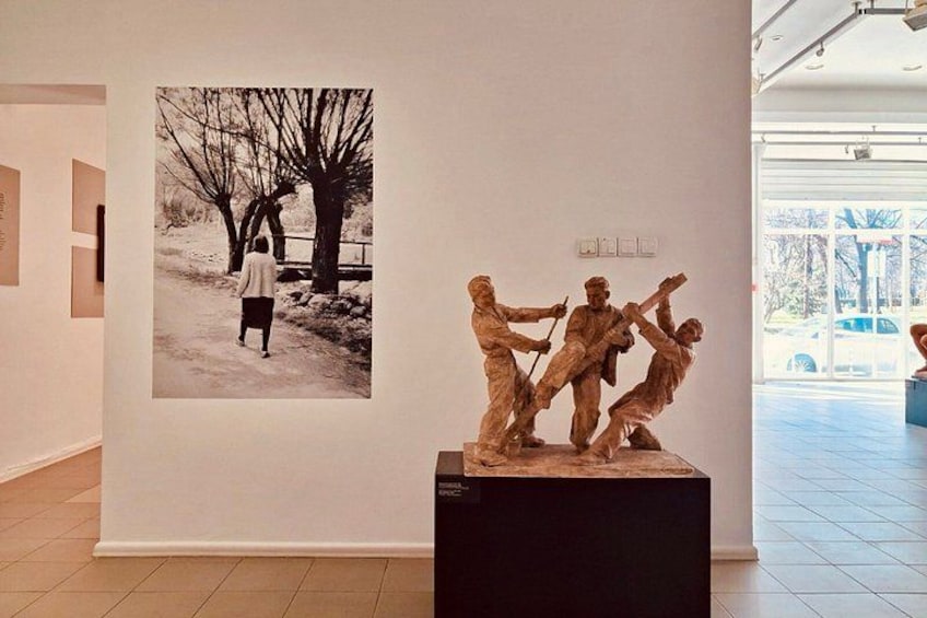A sculpture of three figures on a pedestal, a black and white photograph on the wall, and a modern interior space. 4