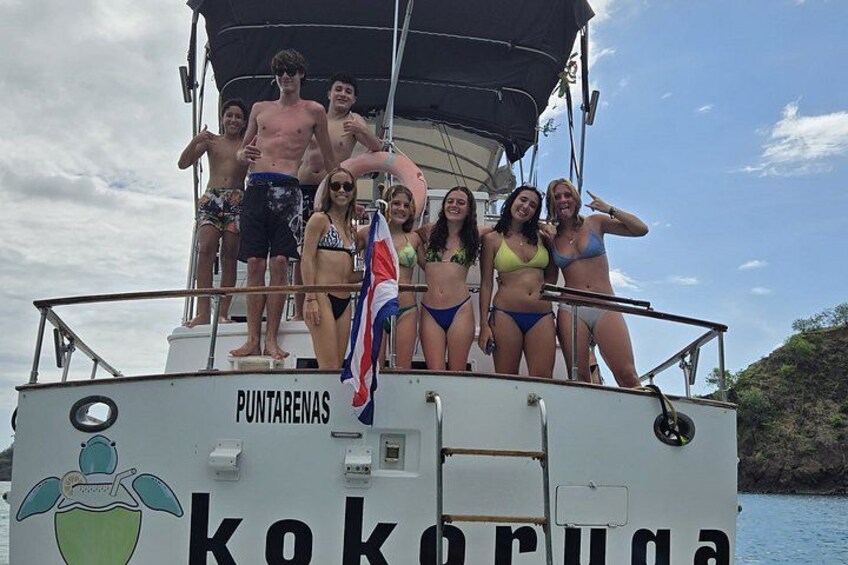 Eine Gruppe von Menschen auf einem Boot, auf dessen Seite die Namen 'Puntarenas' und 'kokoruga' zu sehen sind. 3