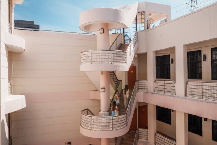 A multi-level atrium with a central spiral staircase, multiple balconies, and a clear sky. 3