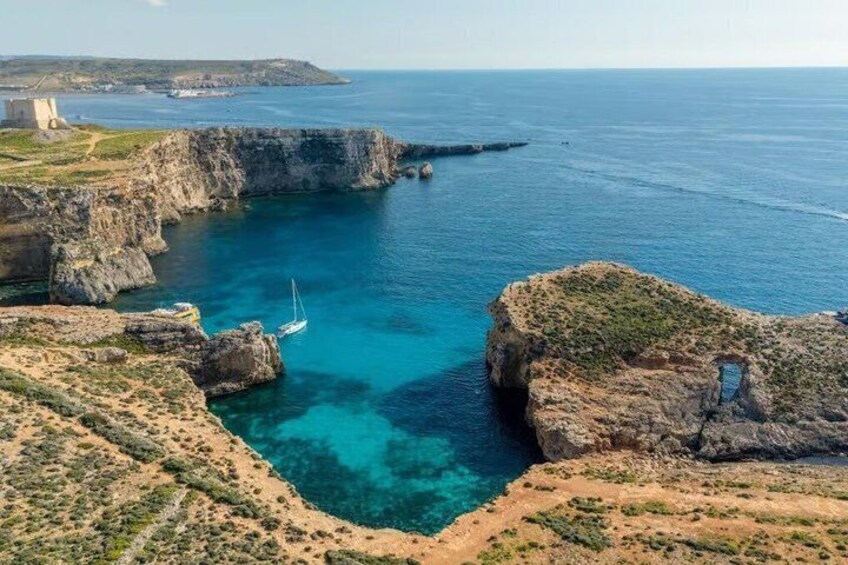 Paesaggio costiero con scogliere rocciose, acque blu cristalline e una barca a vela. 5