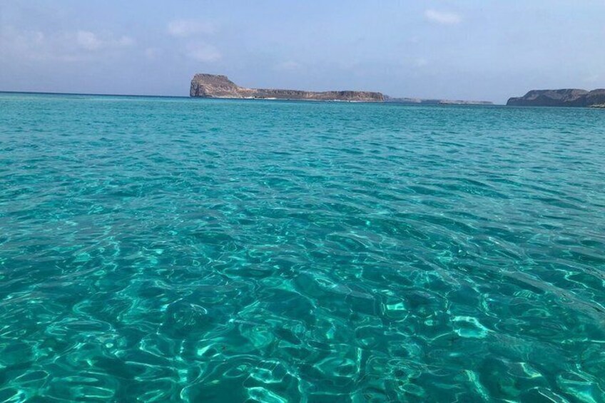 Agua marina turquesa con excelente visibilidad, formaciones rocosas a lo lejos y cielo despejado. 4