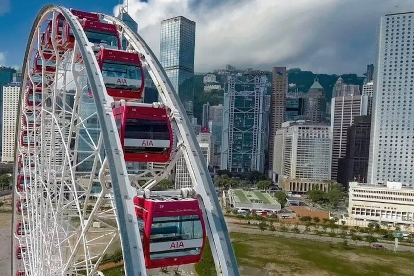 A Ferris wheel with red cabins labeled 'AIA' in a cityscape with modern buildings. 5