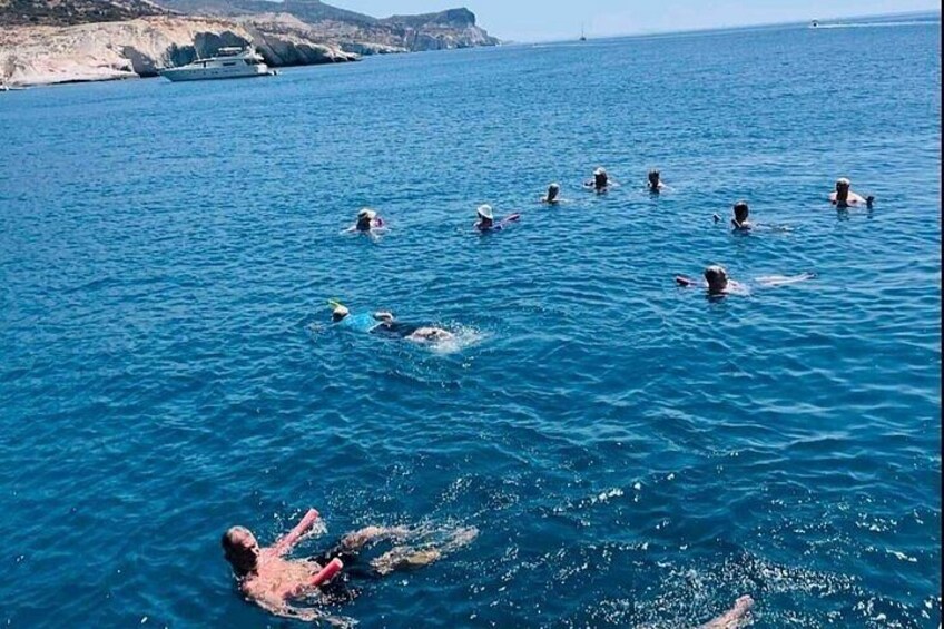 A group of people swimming in a clear blue sea with a boat in the background. 4