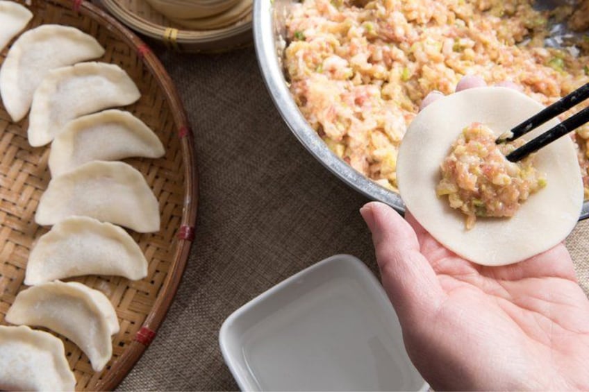 A hand holding a dumpling with chopsticks, a basket of dumplings, and a pan of cooked dumplings. 4
