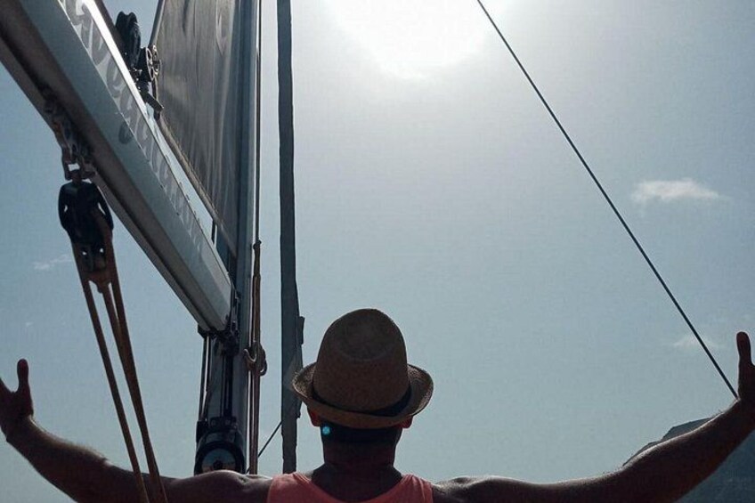 A person on a sailboat with arms outstretched, a hat, and a clear sky. 4