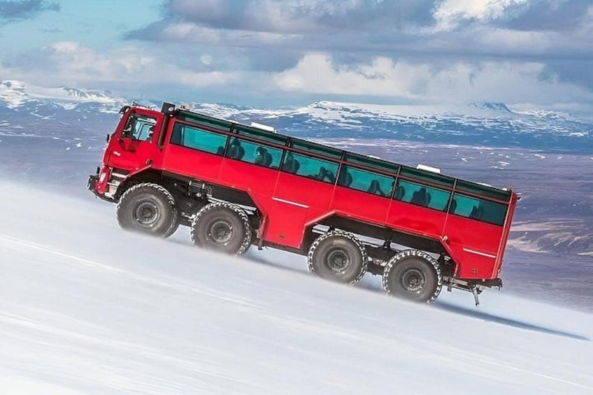 A red truck driving on a snowy road with mountains in the background. 2