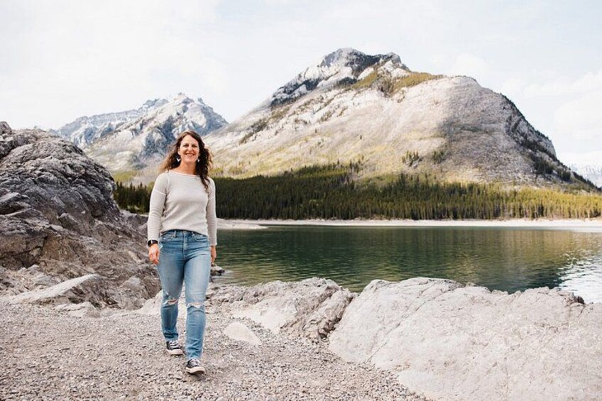 A person standing on a rocky shore with a lake and mountains in the background. 3