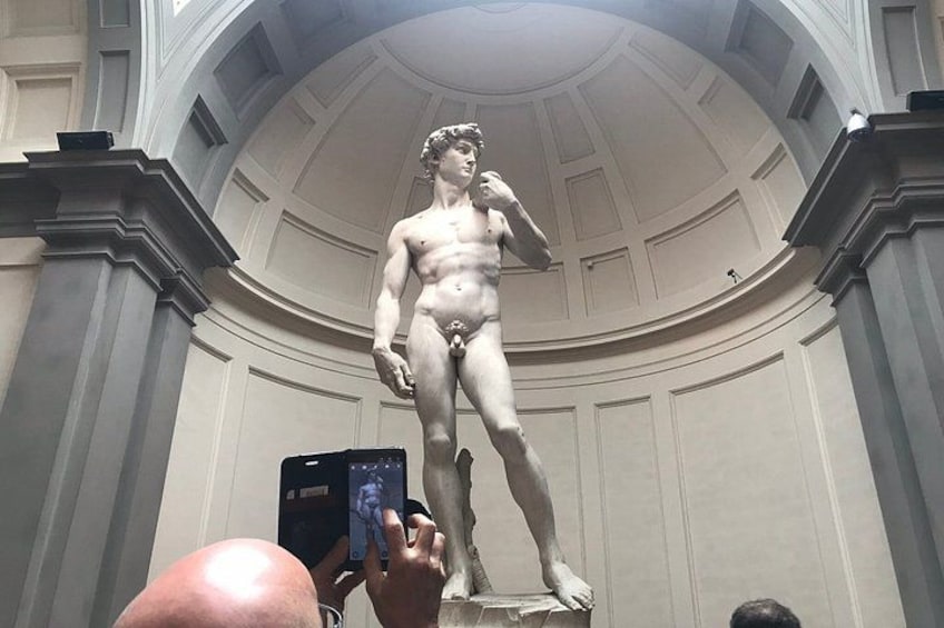Una estatua de mármol de una figura masculina de pie en una pose clásica, con una persona tomando una fotografía. 5