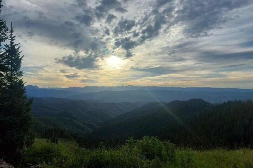 Un paisaje montañoso con el sol ocultándose tras las nubes, rodeado de bosques densos. 1