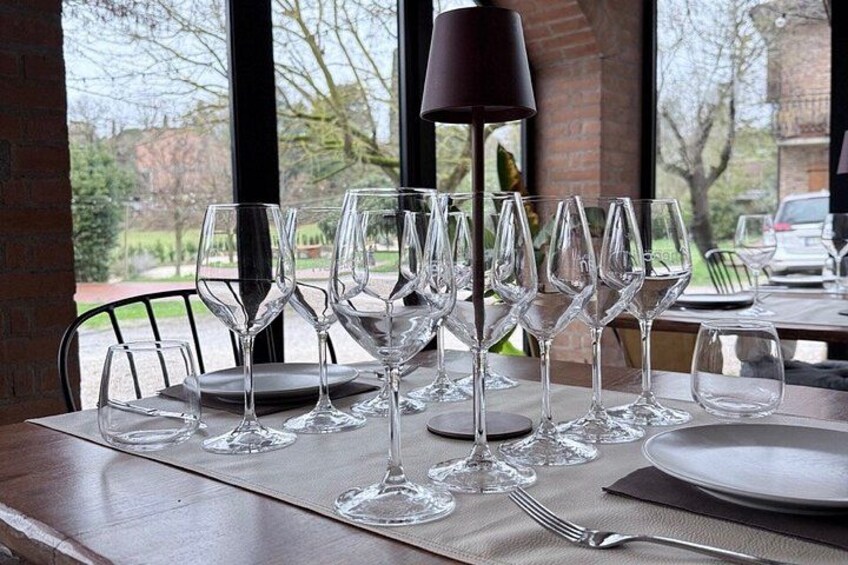 Une table dressée avec des verres à vin et des assiettes, une lampe, et une vue sur un jardin par la fenêtre. 3