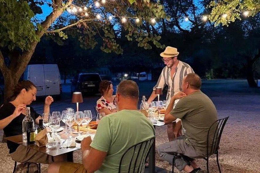 Un groupe de personnes dînant en plein air, la nuit, sous des guirlandes lumineuses. 2