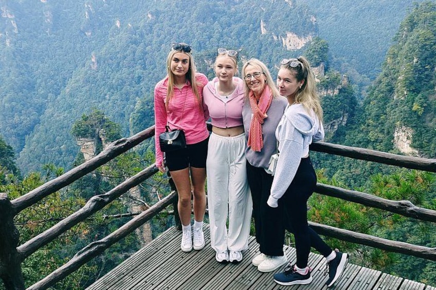 Four people standing on a wooden platform with a mountainous landscape in the background. 3