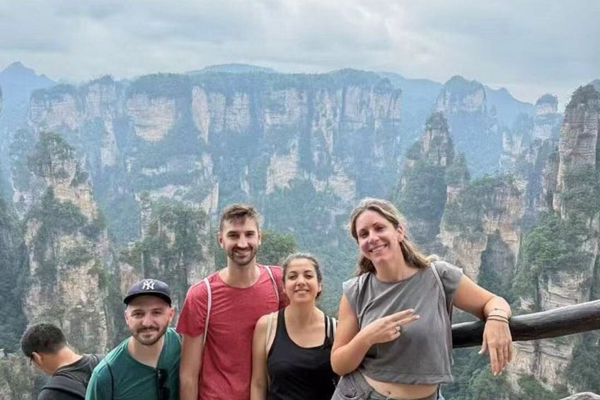 A group of people standing on a viewing platform with a mountainous landscape in the background. 2
