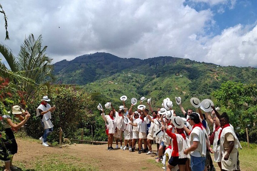 A group of people in white and red attire, some holding hats, standing on a dirt path with a mountainous landscape in the background. 5