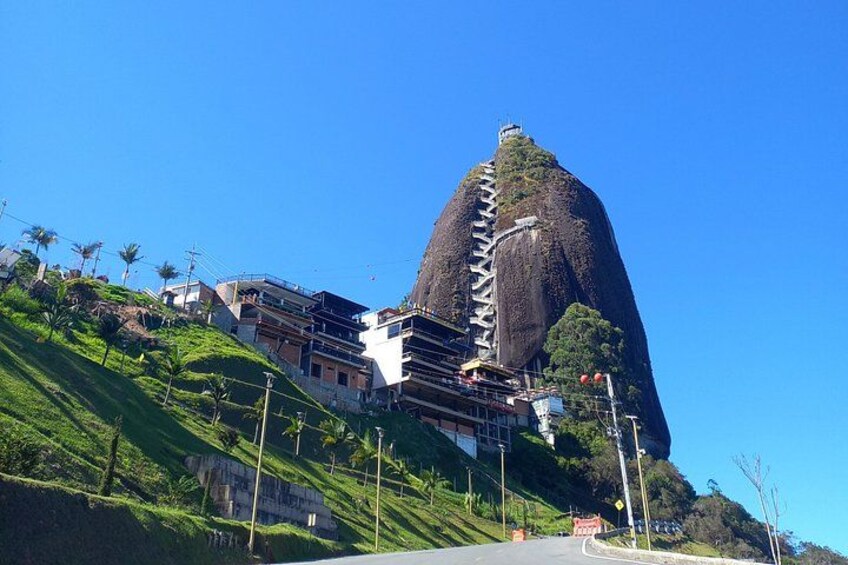 A mountain with a staircase leading to a building, surrounded by greenery and clear skies. 1