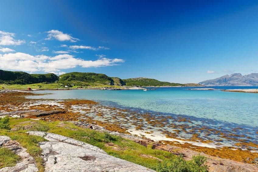A coastal landscape with clear water, rocky shore, and green hills. 5