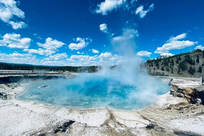 A geyser with steam rising, surrounded by a snowy landscape and a clear blue sky. 2