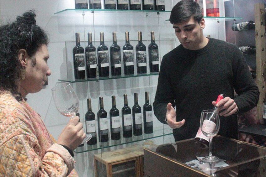 A person holding a wine glass, another person holding a wine bottle, and a display of wine bottles on shelves. 5