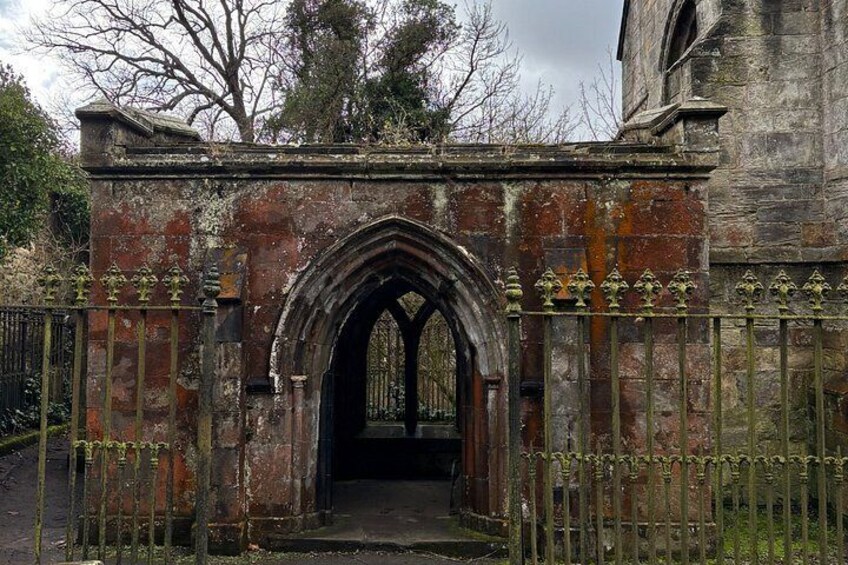 An arched stone gateway with a metal fence, leading into a building with a brick facade. 2