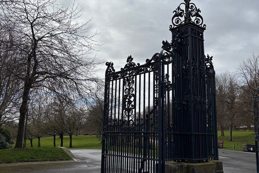 A wrought iron gate with intricate designs, surrounded by leafless trees and a pathway. 4
