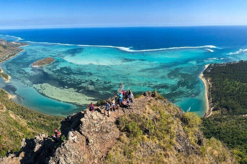 A group of people on a rocky cliff overlooking a turquoise sea with clear waters and a coastline. 1