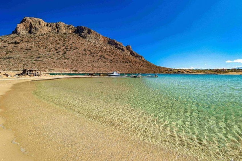 A beach with clear water, a boat, and a mountain. 2