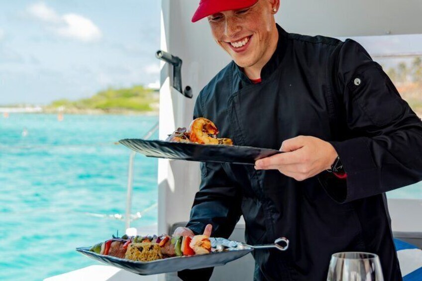 A person serving food on a boat with a clear view of the ocean and distant shoreline. 3
