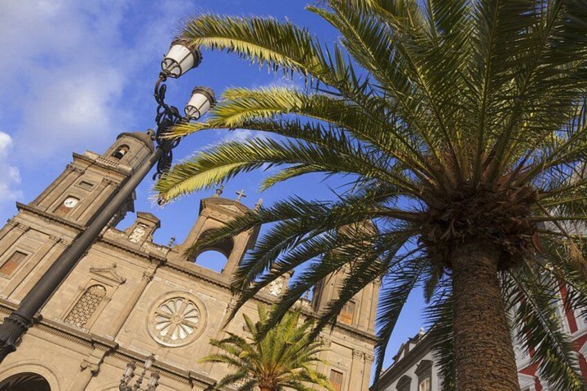 A historic church with a clock tower, palm trees, and a street lamp. 5