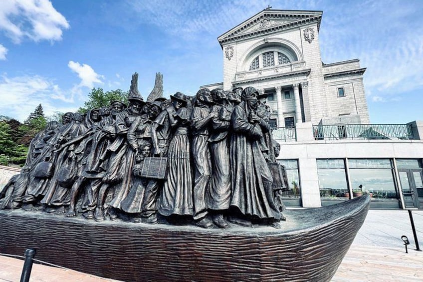 A large bronze sculpture of a crowd in front of a building with classical architecture. 1