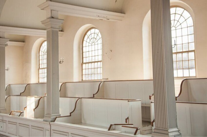 A row of white benches with curved backs and a high ceiling with arched windows. 5