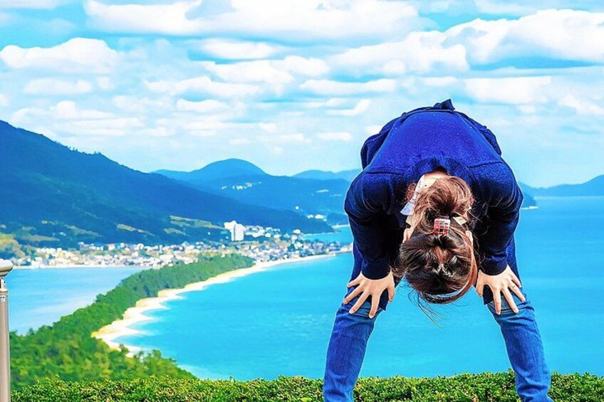 A person performing a yoga pose on a grassy hill overlooking a coastal town with a clear sky. 1