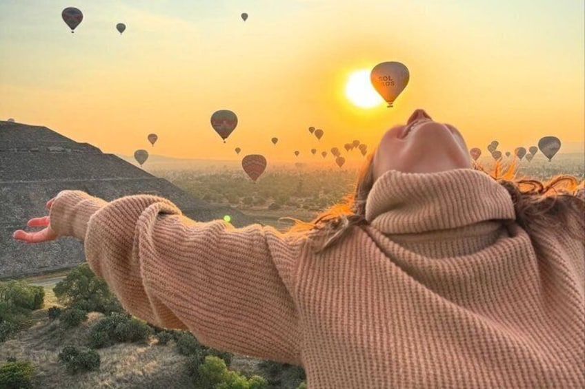A person with outstretched arms, a sunset, and hot air balloons in the sky. 1
