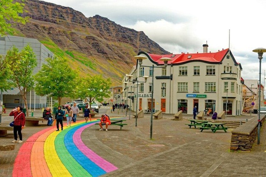 A public square with a rainbow-colored path, benches, and a building with a red roof. 3