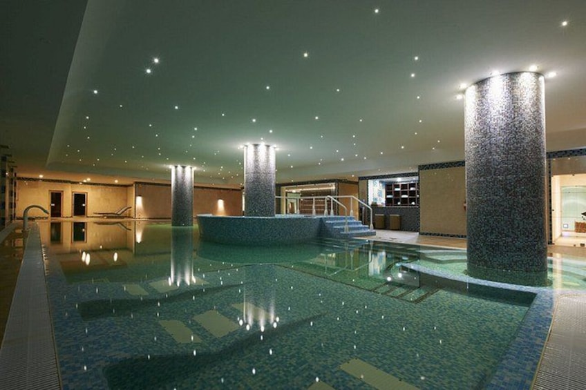 An indoor swimming pool with a tiled floor, surrounded by walls and pillars, and a staircase leading to an upper level. 4