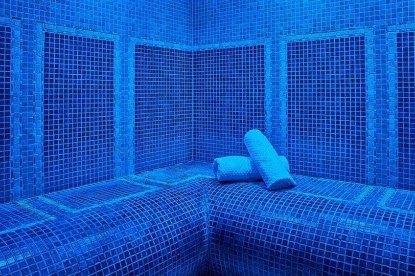 A blue-tiled room with a corner sofa and two rolled-up cushions. 1