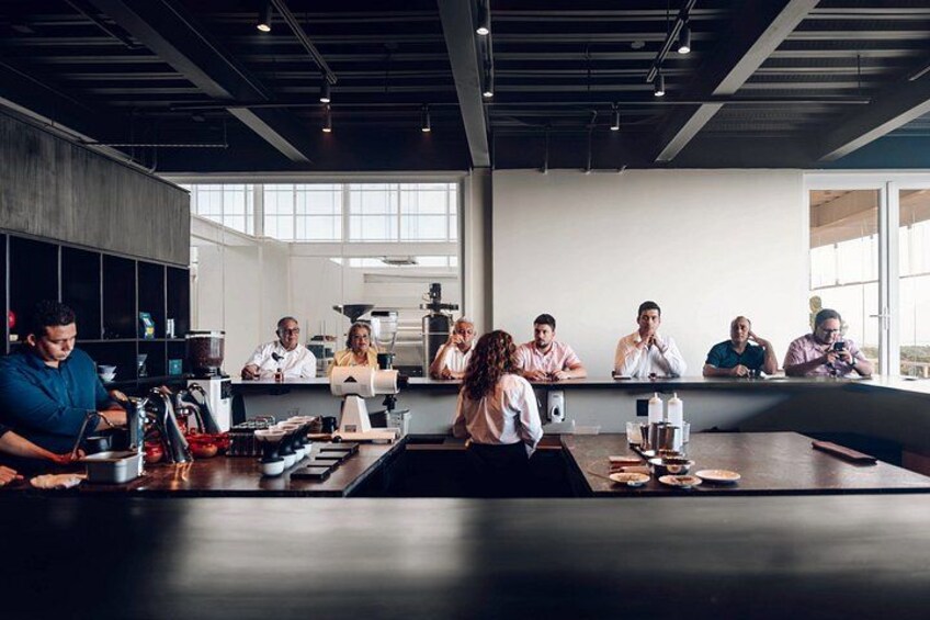 Un grupo de personas en una cocina moderna con una mesa larga, equipo de cocina y ventanas amplias. 1