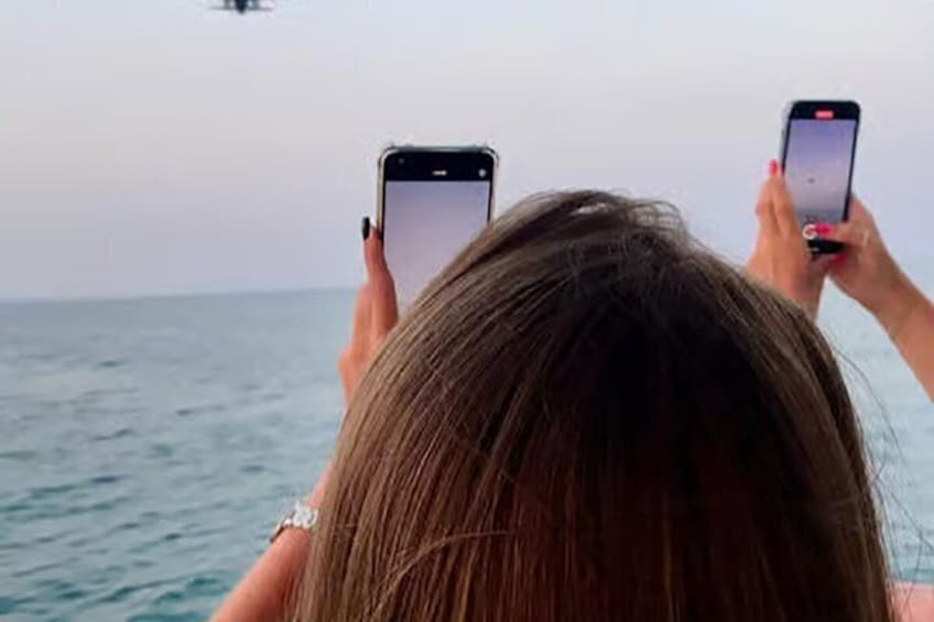 A person holding two smartphones, facing the ocean. 5