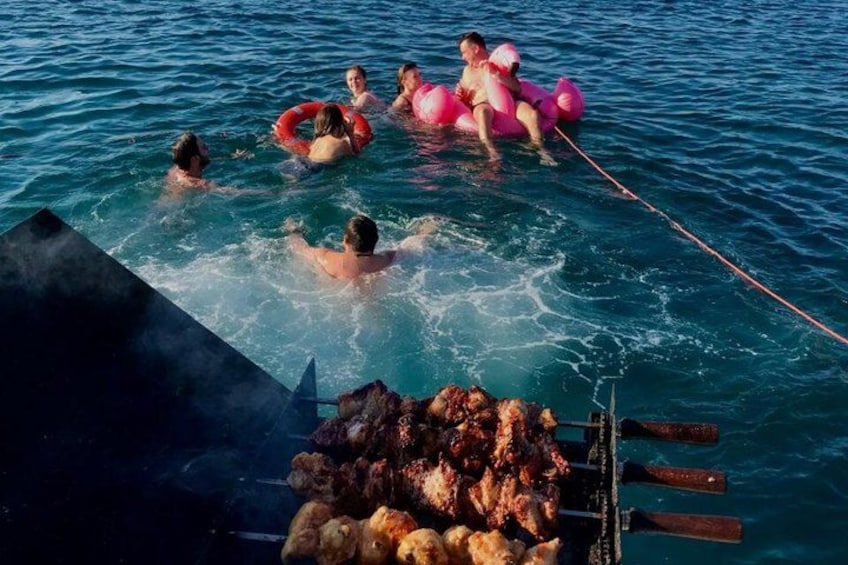 People swimming in a body of water, a grill with food, and a rope. 2