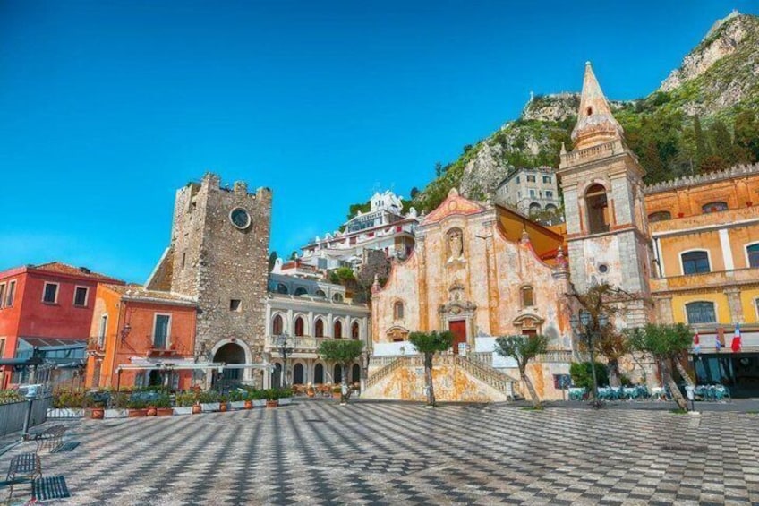 Eine historische Stadt mit einem markanten Turm, farbenfrohen Gebäuden und einem gepflasterten Platz. 3