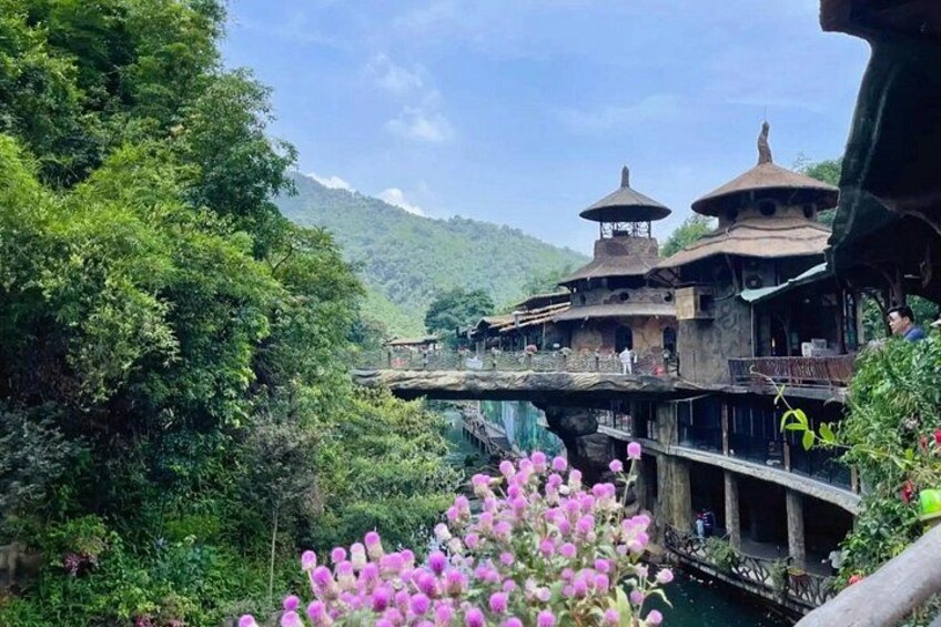 A traditional building with a thatched roof, a wooden bridge, and lush greenery. 4