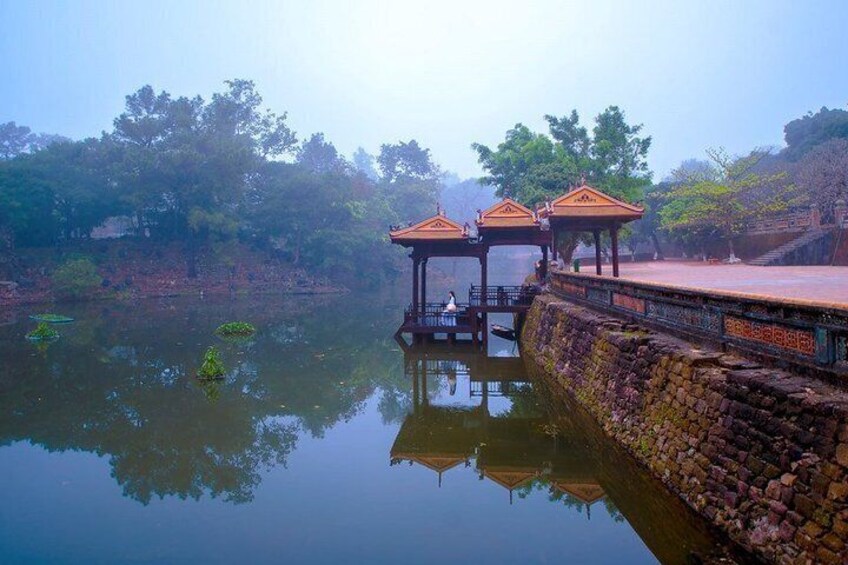 A serene lakeside scene with traditional wooden gazebos and a stone wall. 4