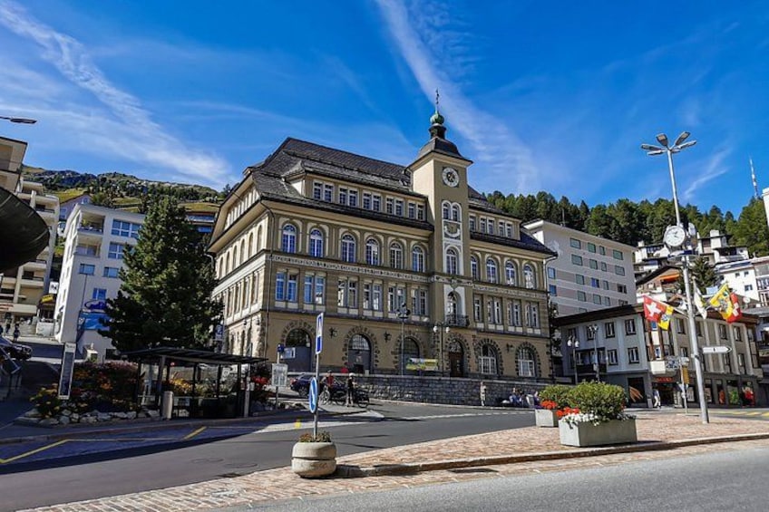 A historic building with a clock tower, surrounded by modern buildings and a clear blue sky. 5