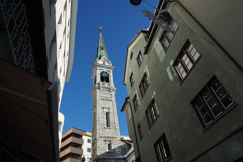 A tall clock tower with a pointed roof, surrounded by modern buildings. 3