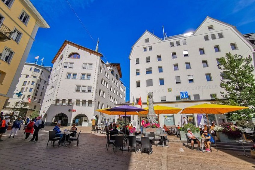 A public square with outdoor seating, buildings, and flags. 2