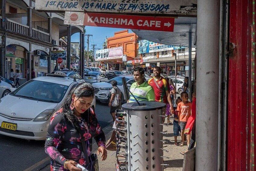 A busy street with a taxi, a woman using a phone, and a cafe named 'Karishma Cafe' with a sign above. 3